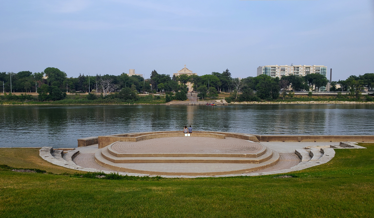 a terrace with a concrete circle at the bottom with a couple sitting on its wall facing a river