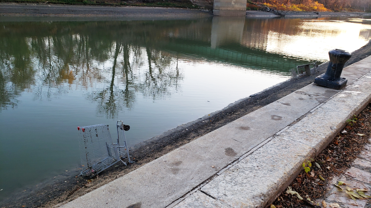 a riverbank at dusk next to a dock with a low river level exposing two shopping cars that have returned to their homeland