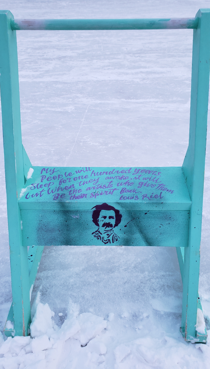 a wooden walker (the kind meant to help people ice skate) painted a light blue with Louis Riel's face spray painted in black through a stencil. There is text on the seat of the walker saying 'My people will sleep for one hundred years but when they awake it will be the artists who give them their spirit back - Louis Riel'