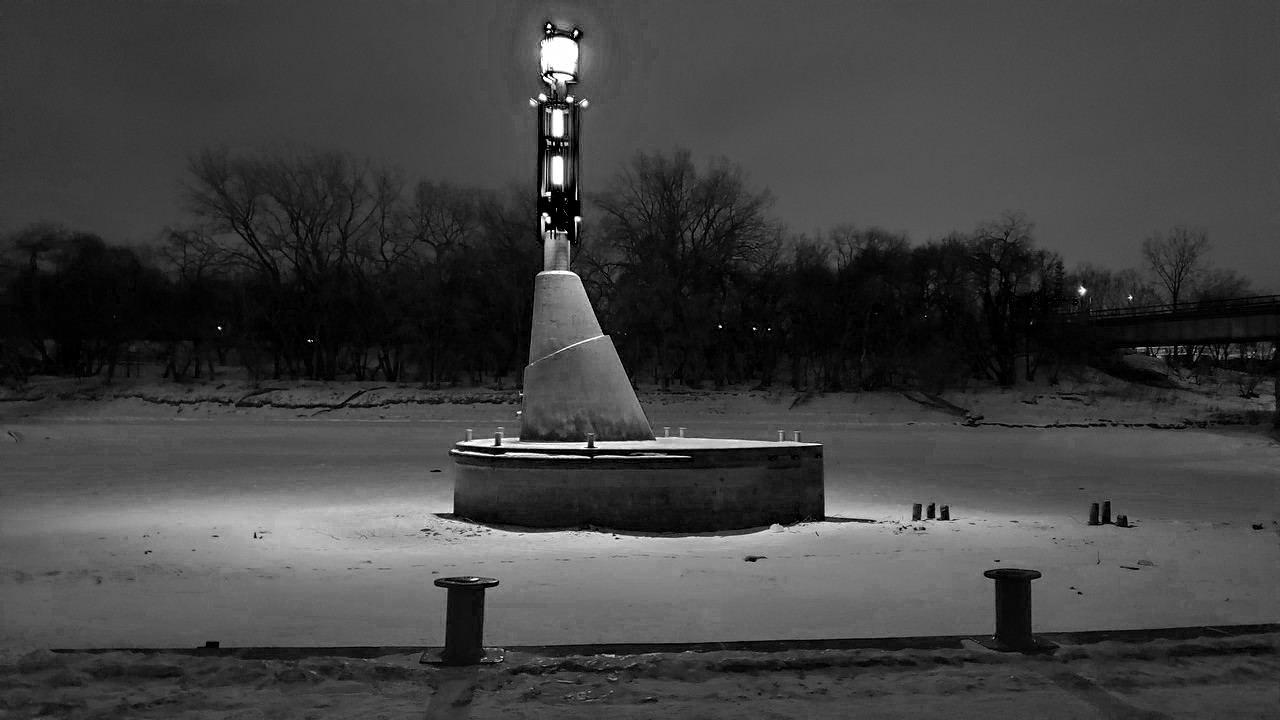 a black and white photo of a a light on top of a pole on a concrete plaform in a river by the pier