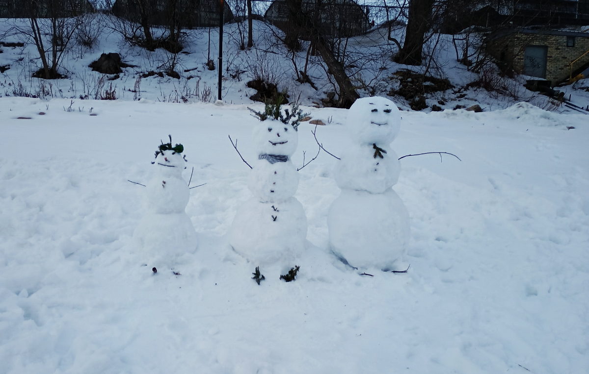 a family of snow people built upon a riverbank, from the perspective of standing on the frozen river