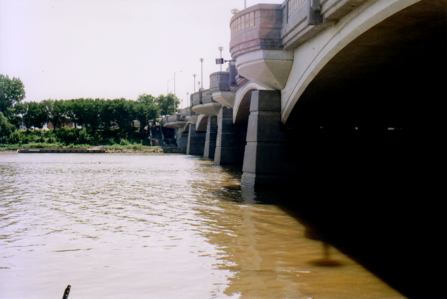 a grainy film photo of yellow water under a stone bridge