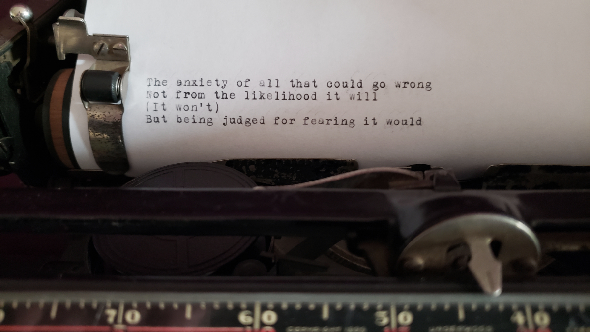 a piece of paper in an old school typewriter saying: The anxiety of all that could go wrong / Not from the likelihood it will / (It won't) / But being judged for fearing it would.