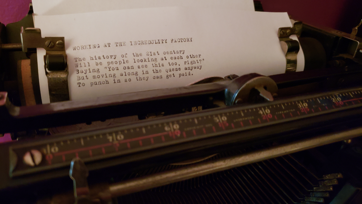 a piece of paper in an old school typewriter saying: WORKING AT THE INCREDULITY FACTORY / The history of the 21st century / Will be people looking at each other / Saying 'You can see this too, right?' / But moving along in the queue anyway / To punch in so they can get paid.