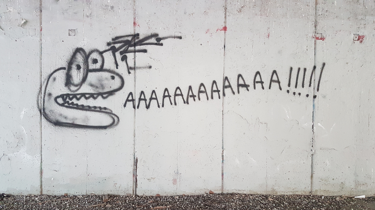 a concrete wall with a lizard-like cartoonish head drawn on the left screming 'AAAAAAAAAAAA!!!!!' with the letters going across the frame of the picture