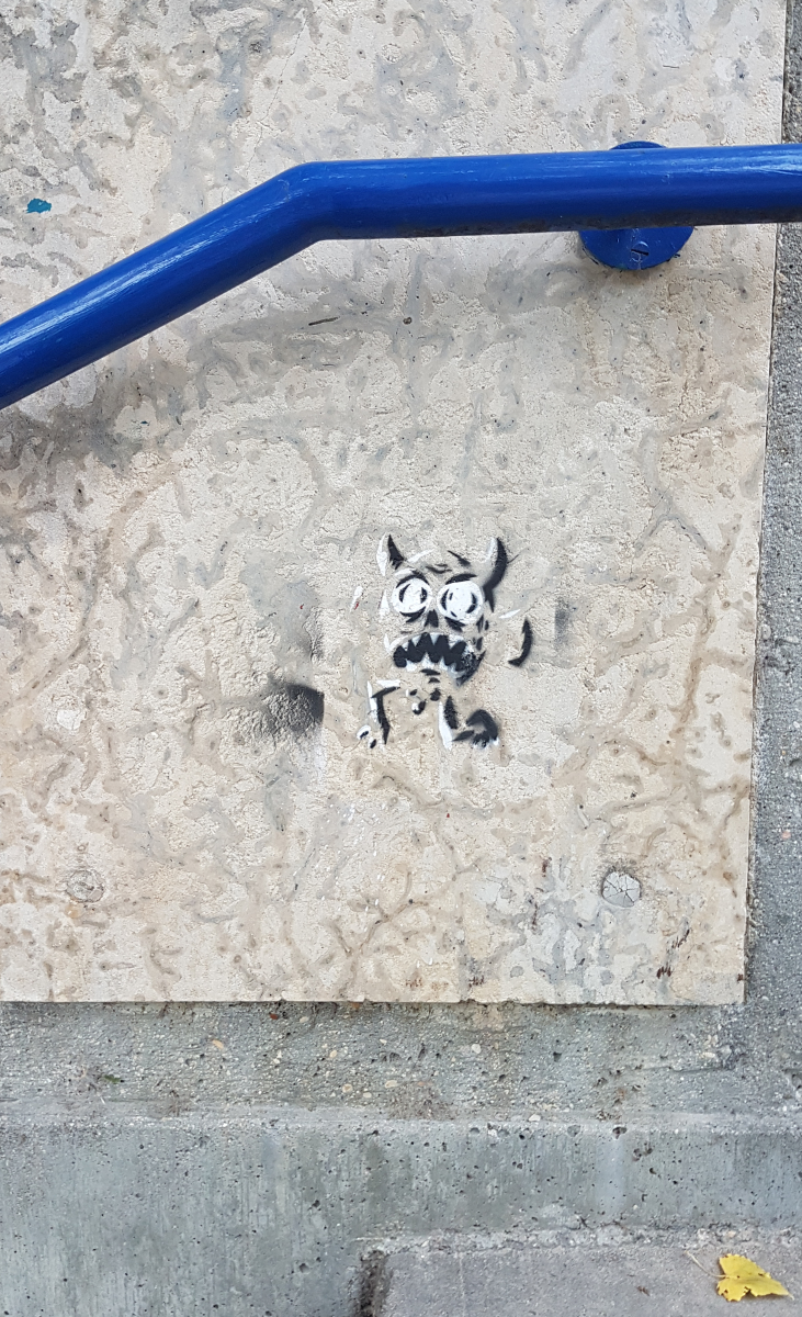 a stone wall with a blue metal railing on it above concrete steps with a stencil of a black and white devil painted on it