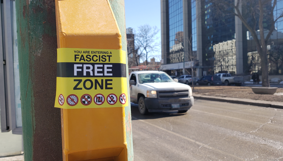 A sticker on a traffic pole saying 'you are entering a fascist free zone' with various fascist symbols at the bottom with red circle no signs over them