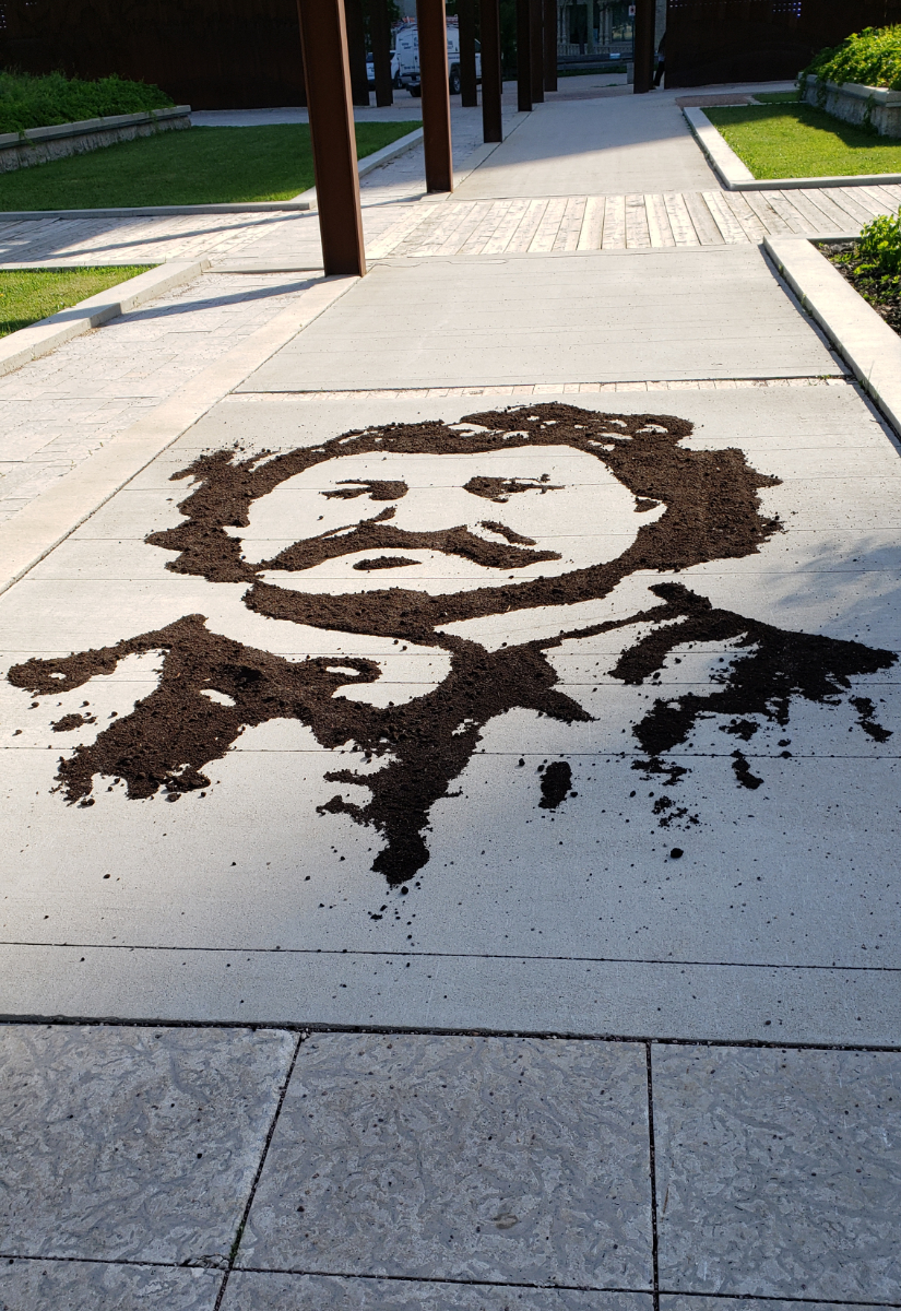 The sidewalk in a park with dirt spread about to form a portrait of Louis Riel, Métis leader and founder of Manitoba.