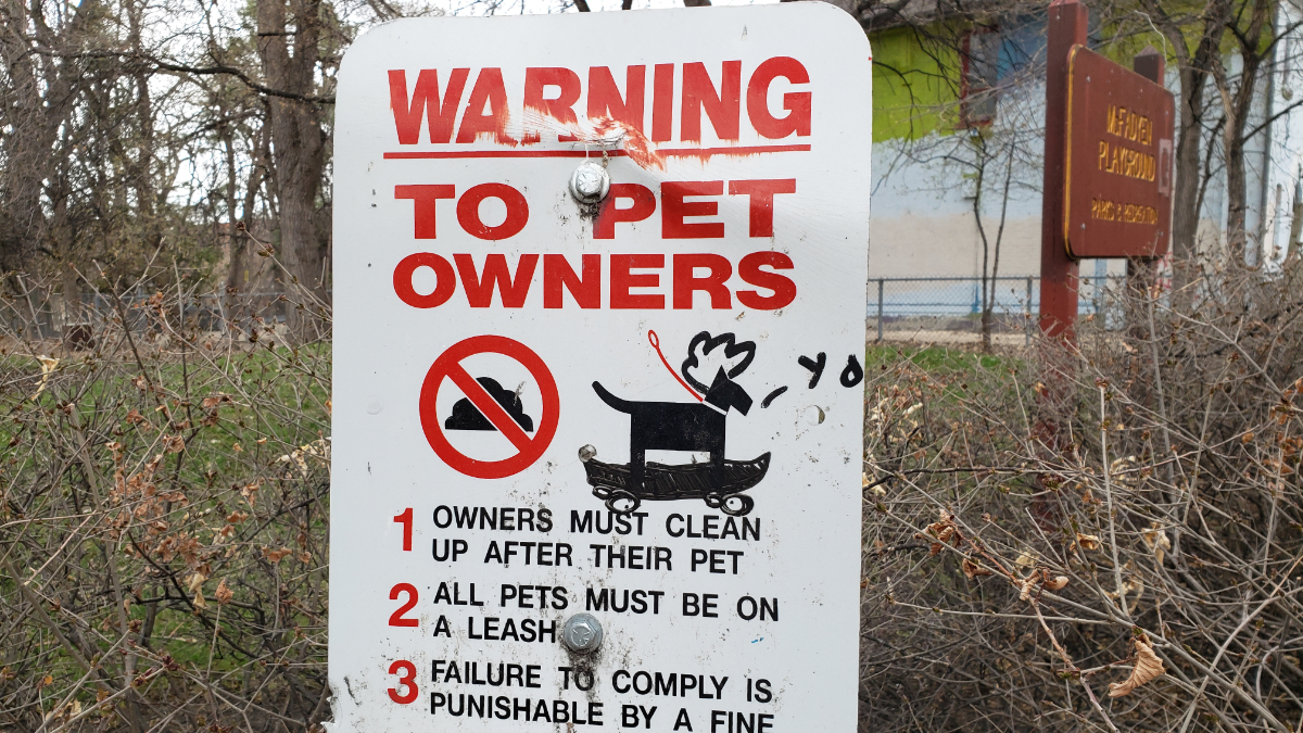 a park sign saying 'WARNING TO PET OWNERS' with your standard rules about leashes and pickign up shit, but the icon of the dog on the sign has a white afro doodled onto his head and he is riding a skateboard while saying 'yo'