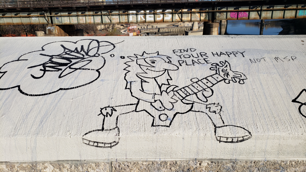 the top of a concrete wall on a bridge with a cartoon 80s-era rock star guitarist drawn in black marker. there's a thought bubble to the left with a gibberish tag written in, and to the right it says 'find your happy place' (someone else has written 'not MSP' next to that).