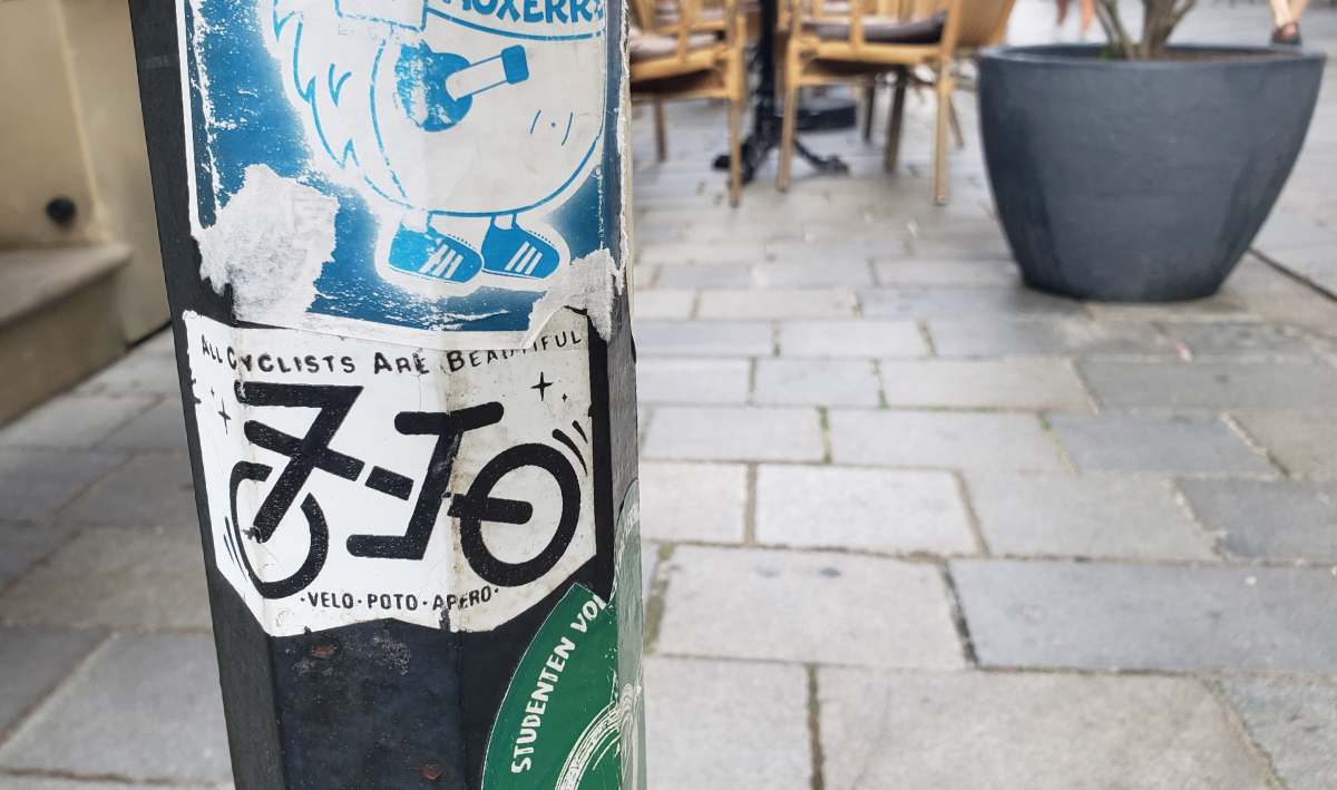 a lamppost with a sticker featuring an icon of a bicycle with 'all cyclists are beautiful' written above it