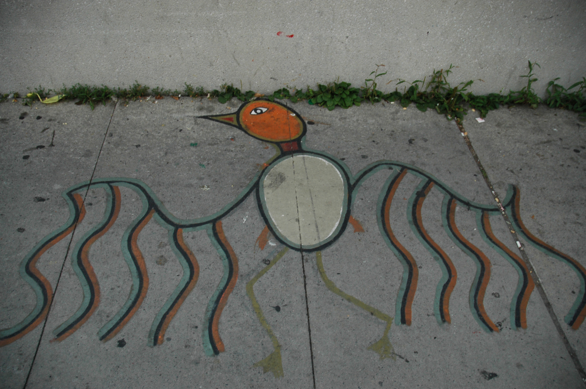 a sidewalk with a bird painted on it in an Indigenous Turtle Island motif, using mostly orange and teal colours