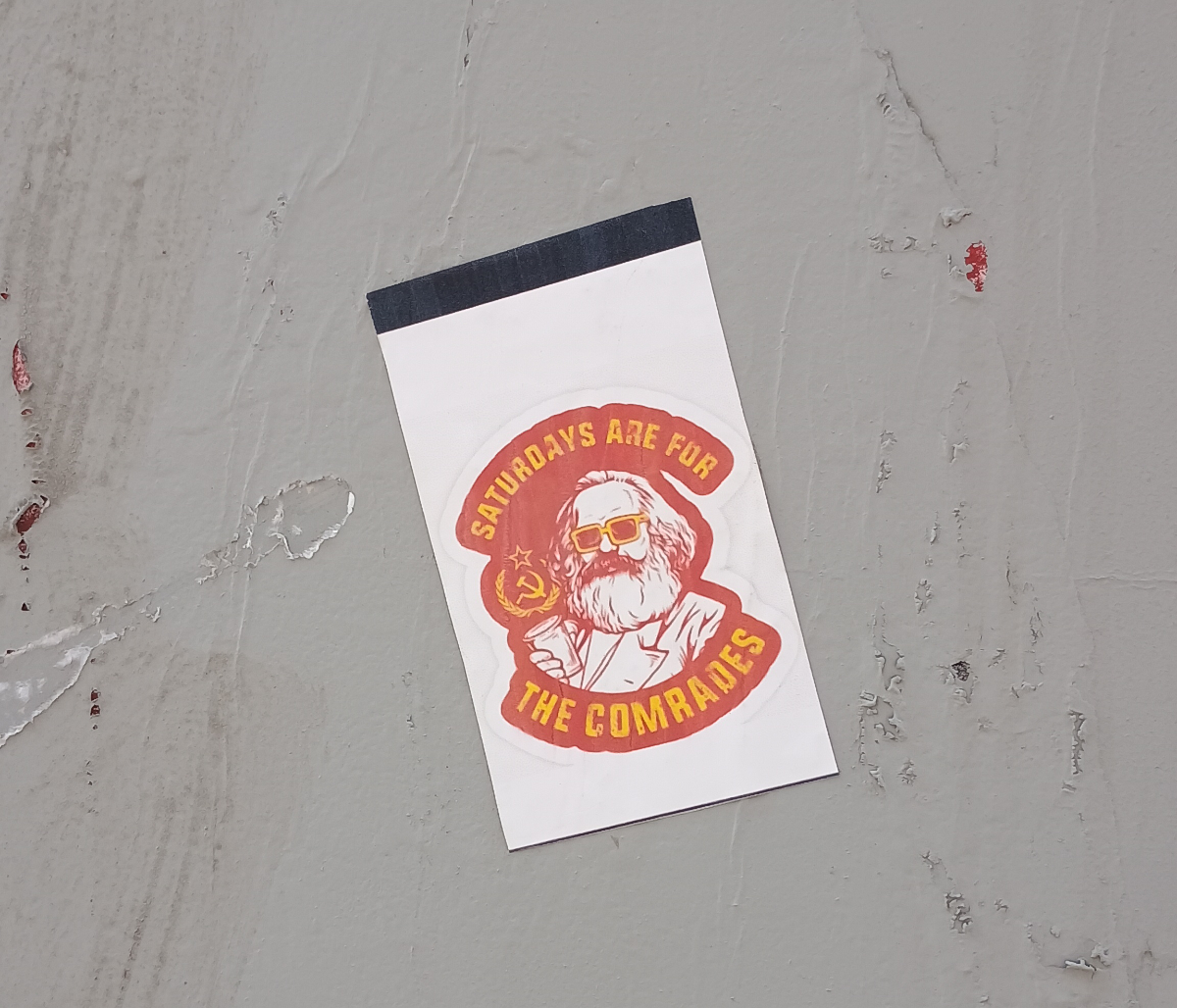 Winnipeg a greywall with a white and red sticker with Karl Marx wearing sunglasses and holding a cup with the words 'Saturdays are for the comrades' around him and a hammer and sickle logo in yellow