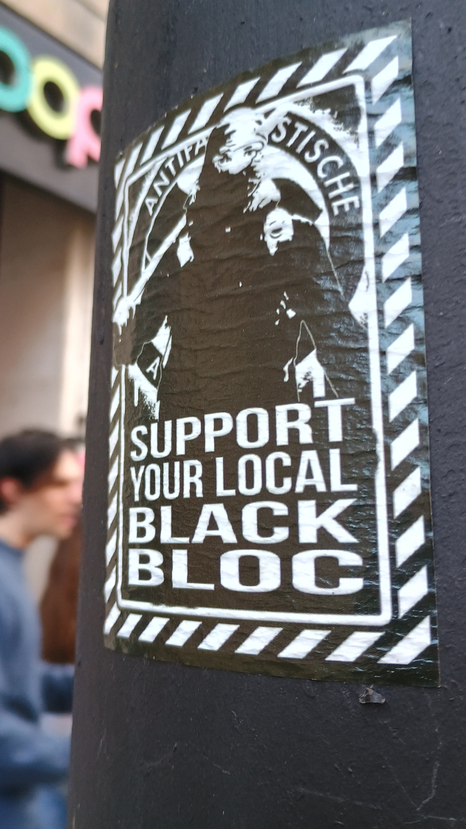 Bristol, UK a curved black-painted concrete surface with a black and white poster of a person in black clothes and a balaclava with the text 'support your local black bloc'