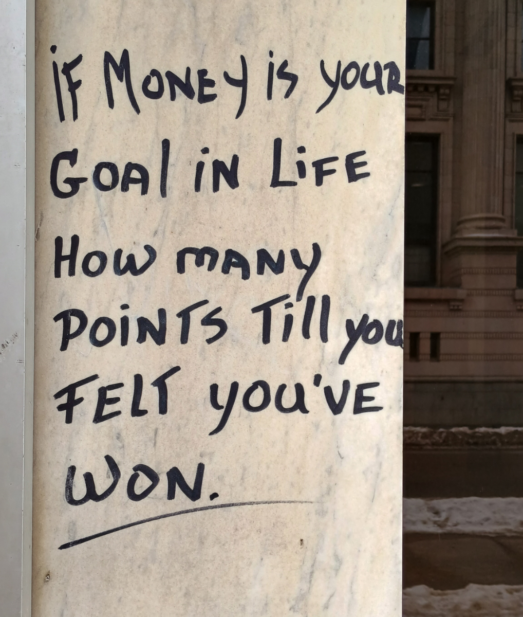 a stone pillar with black handwriting saying 'if money is your goal in life how many points till you felt youve won?'