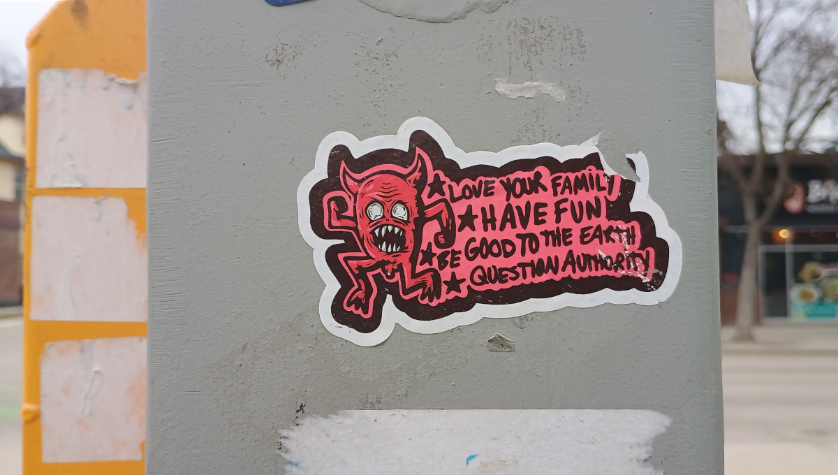a grey box with a sticker on it featuring a demon character with a dick sticking out between the legs, with a caption saying 'love your family, have fun, be good to the earth, question authority'
