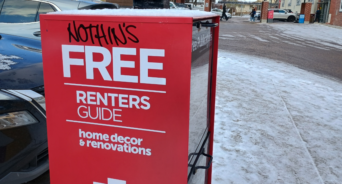 parking lot with a red box that holds free apartment listings and reno guides, but somebody's written 'nothin's' above the word 'free'