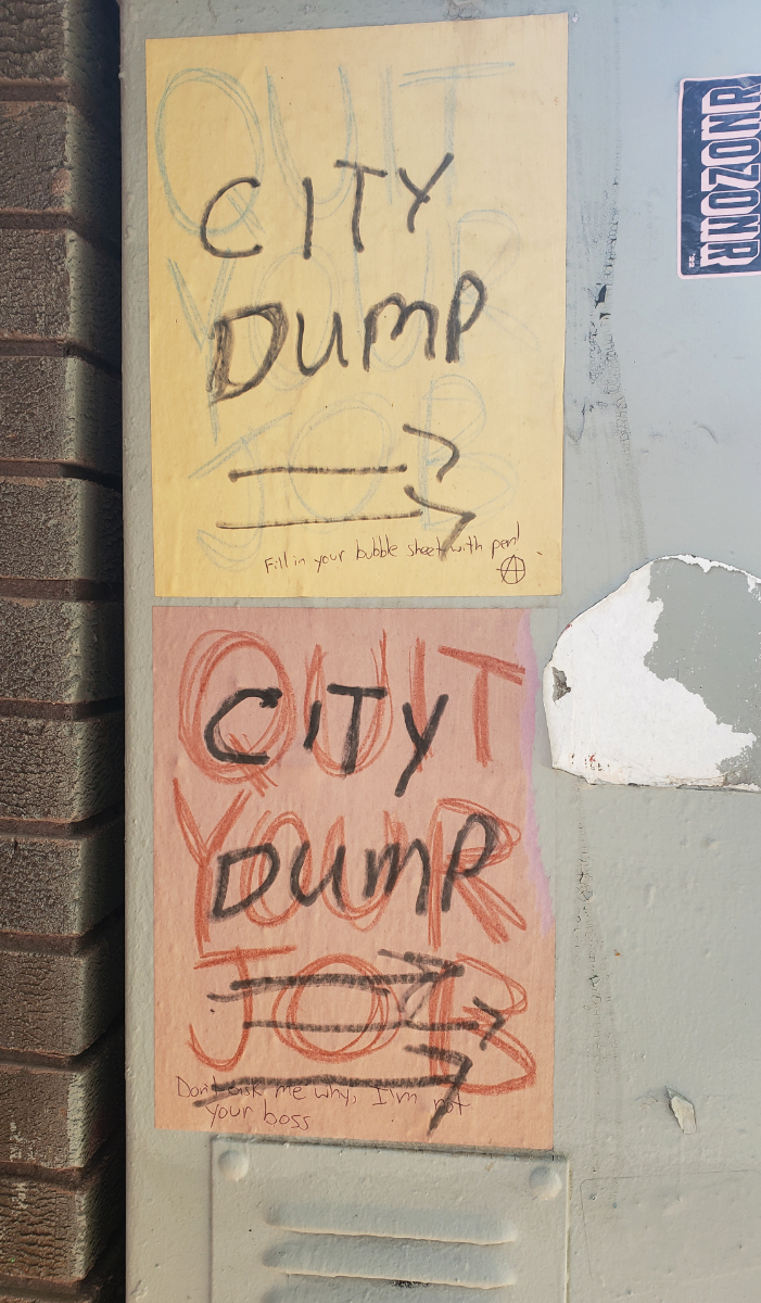 A grey metal surface next to a brick wall that has two QUIT YOUR JOB posters with 'Fill your bubble sheet with pen! (Anarchy symbol)' and 'Don't ask me why, I'm not your boss' messages written on them in pen, but also 'CITY DUMP' with side arrows pointing to the right written over top of these in permanent marker. Boo fucking hoo, buddy.