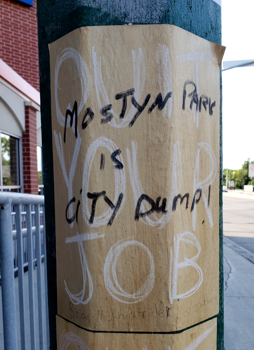 'Mostyn Park is City Dump!' written over a QUIT YOUR JOB sign with 'Brian McKnightrider' in pen