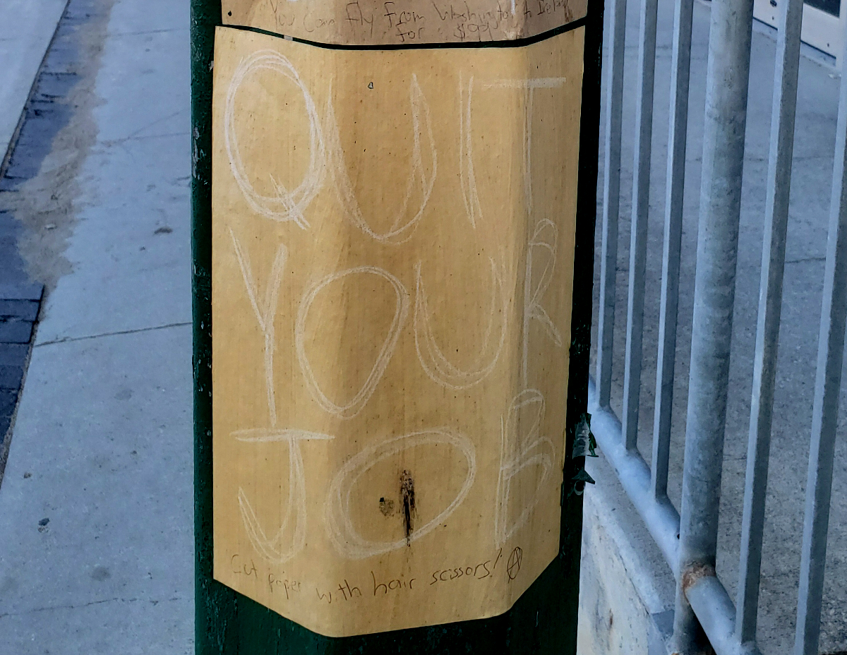 QUIT YOUR JOB sign on a lamppost with 'Cut paper with hair scissors!' and the anarchy symbol in pen