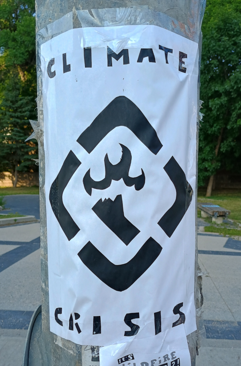a white poster with a black diamond-shaped border cut into four corners like a safety warning sign, within it the outline of the province of Manitoba with a flame over it, and the caption 'climate' on top and 'crisis' below