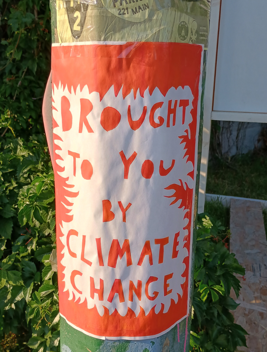 a red poster with a white space inside surrounded by flame-like borders of the red background, and red blocky handwritten text saying 'brought to you by climate change' in the middle