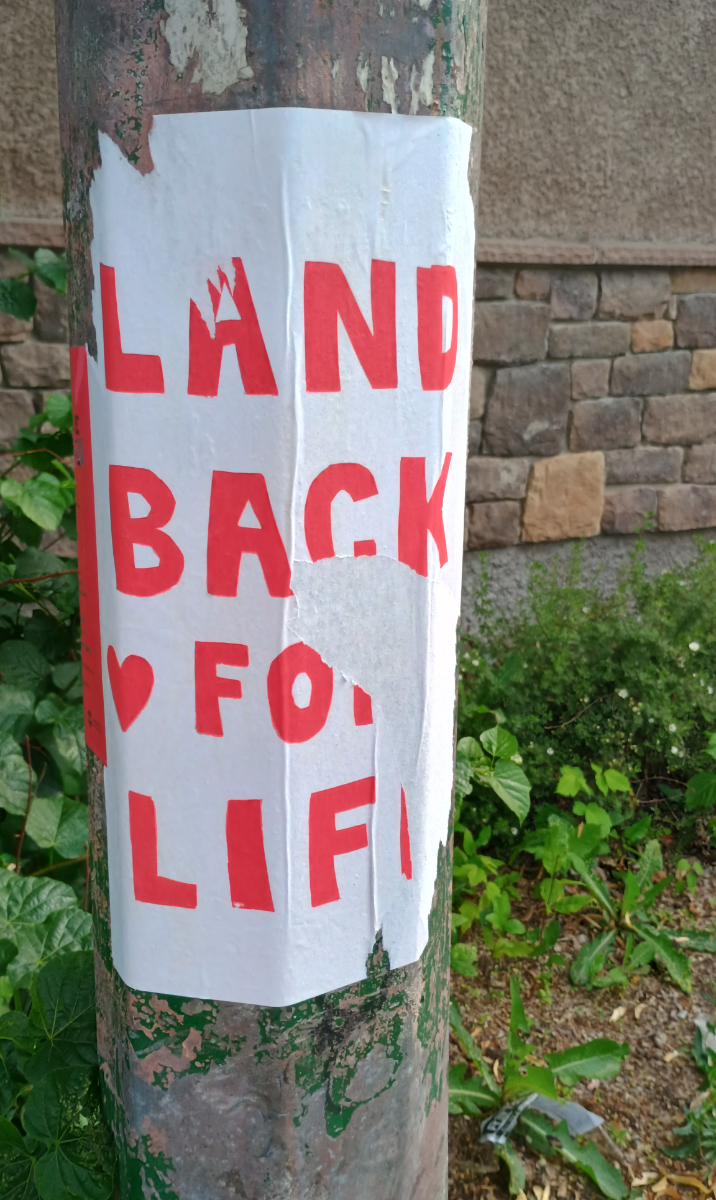 a white poster with red text saying 'land back for life' but somebody's tried to peel the poster off so parts of the letters are missing