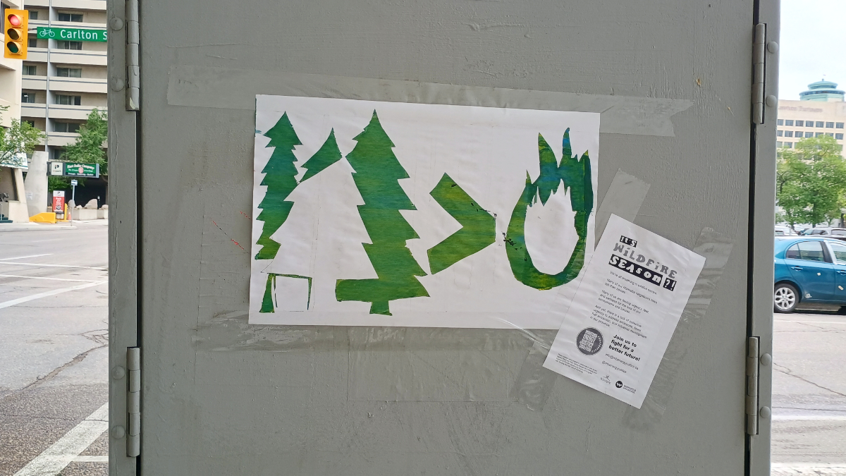 A white poster on a grey power box with a city street in the background. The poster has green silhouette shapes showing trees as being greater than tire