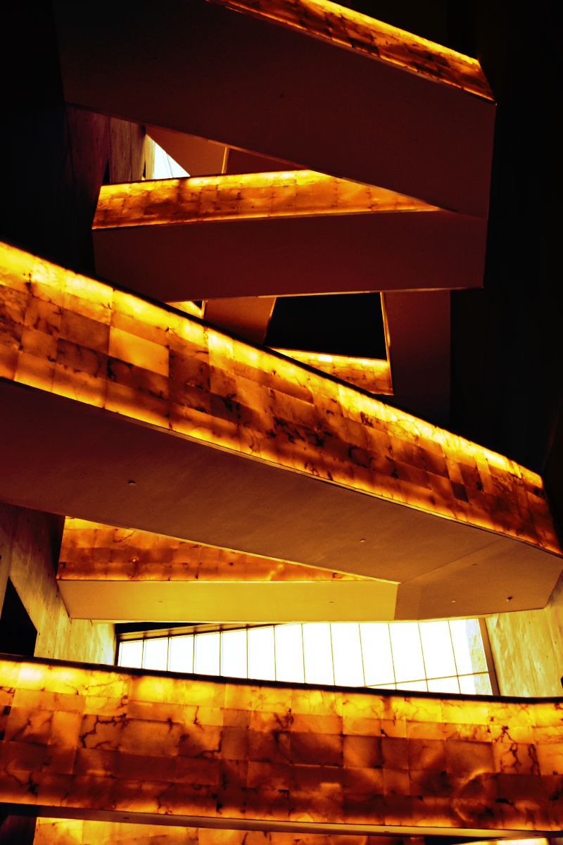 bridges of walkways going up several floors with windows in the background, recoloured with a fiery hue. these are within the Canadian Museum of Human Rights, which isn't really saying much on this subject these days.