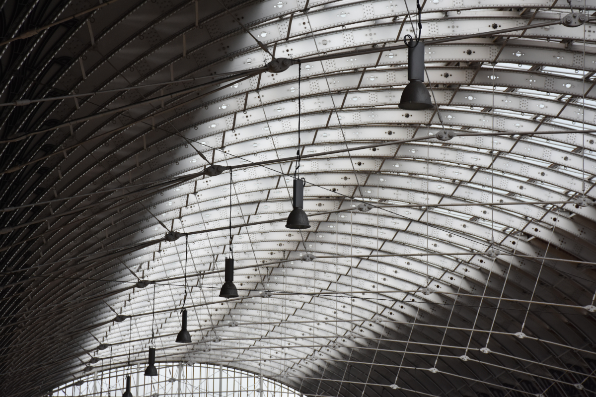 A curved translucent roof of a large semi-indoor space with metal rafters and lamps.